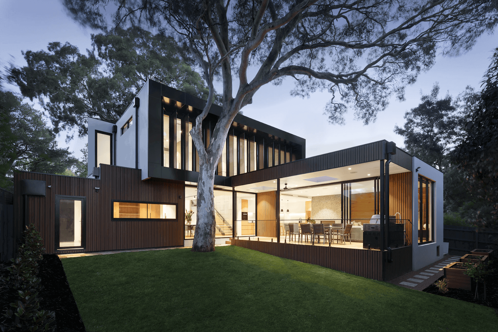 modern-looking home with a tree in the foreground and a green lawn