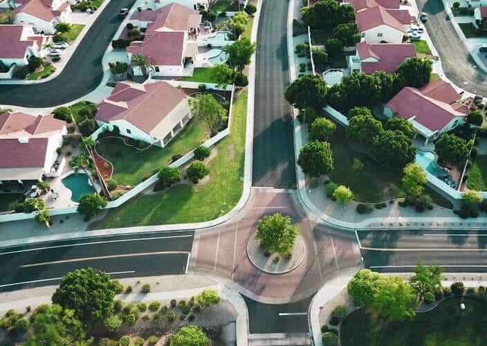 Birds eye view of a roundabout with a tree in midst of a suburban neighborhood in spring, with small white identical houses and green lawns scattered around