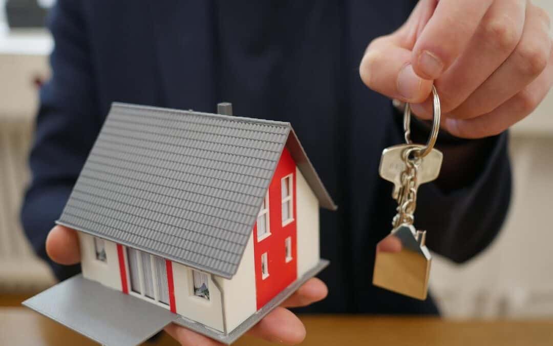 A realtor holding a tiny house prop in one hand and house keys with a metal house-shaped keychain in the other